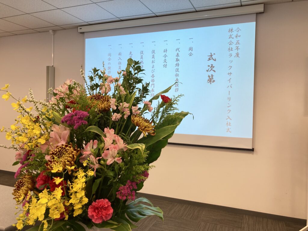 入社式の式次第が投影されたスクリーンと壇上花